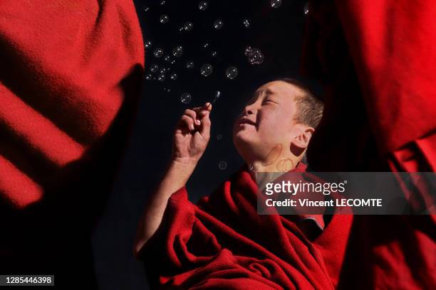Un enfant tibétain vêtu de rouge souffle des bulles de savon dans un monastère lors d'une récréation entre deux séances de prières, décembre 2017,...