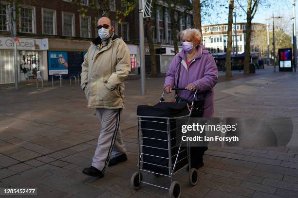 Couple wearing face masks walk through Hull city centre on November 13, 2020 in Hull, England. Hull recorded 726.8 new cases per 100,000 people in...