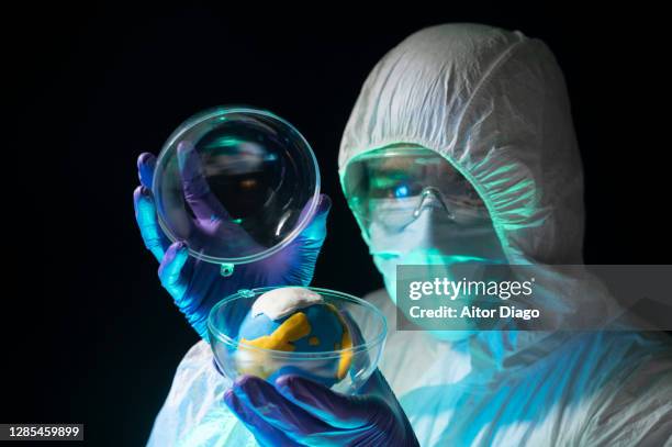 climate change: a scientist in a protective suit cover the planet earth with crystal ball. creative image - climate change health stock pictures, royalty-free photos & images