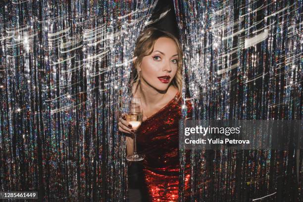 a beautiful blonde girl in a red shiny dress celebrates the new year rejoices smiles lights sparklers drinks champagne - tinsel - fotografias e filmes do acervo