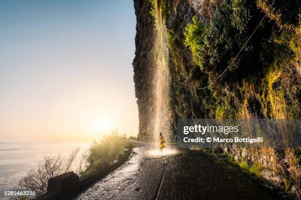 woman playing under waterfall in the middle of the road - madeira fotografías e imágenes de stock