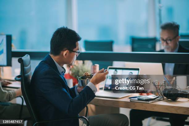 asian chinese young businessman video call working in office and having his meal nasi lemak at his work place having business meeting online with his customer - eating in cubicle stock pictures, royalty-free photos & images