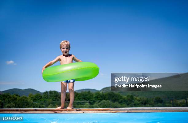 small boy with rubber ring standing by swimming pool in backyard. - very young tube stock-fotos und bilder