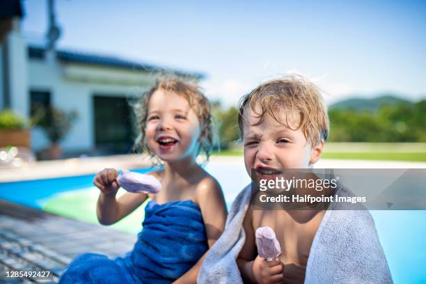 happy small children sitting by swimming pool in backyard, eating ice lollies. - hot boy pics stock-fotos und bilder