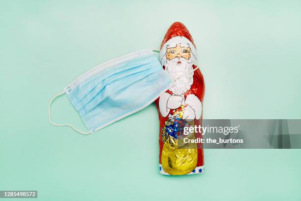 high angle view of a protective face mask and santa claus chocolate on turquoise background - schokonikolaus stock-fotos und bilder