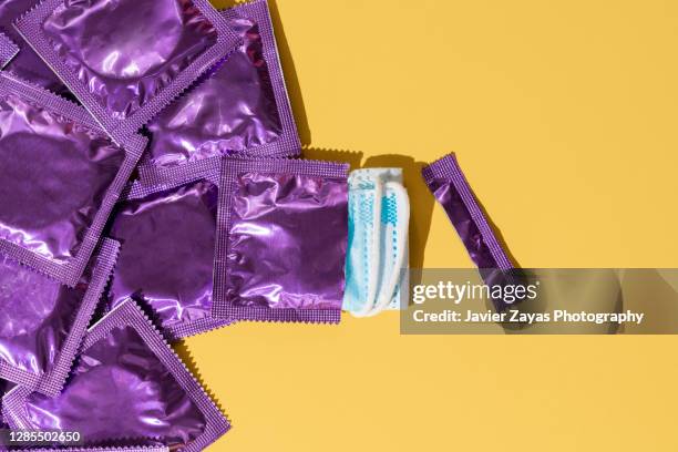 face mask inside a purple condom wrapper on yellow background - kondome stock-fotos und bilder