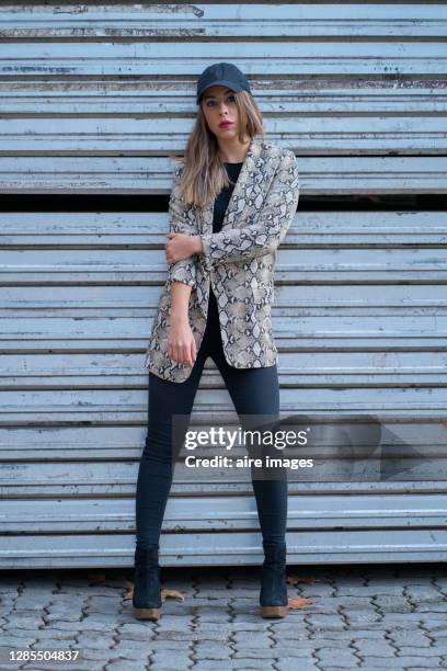 portrait of a young woman wearing a baseball cap and a leopard blazer on a sheet metal background - black leopard stock-fotos und bilder