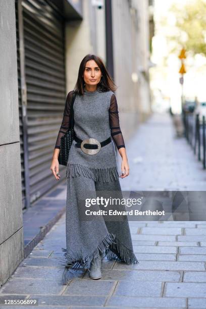 Geraldine Boublil wears a gray sleeveless long wool pullover with fringes, a top with black mesh sleeves, a black leather belt with a large metallic...