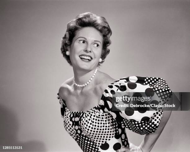 1950s Smiling Woman Looking Over Her Shoulder Posing Wearing Low Cut Scoop Neckline Dress With Polka Dots And Puffy Sleeves