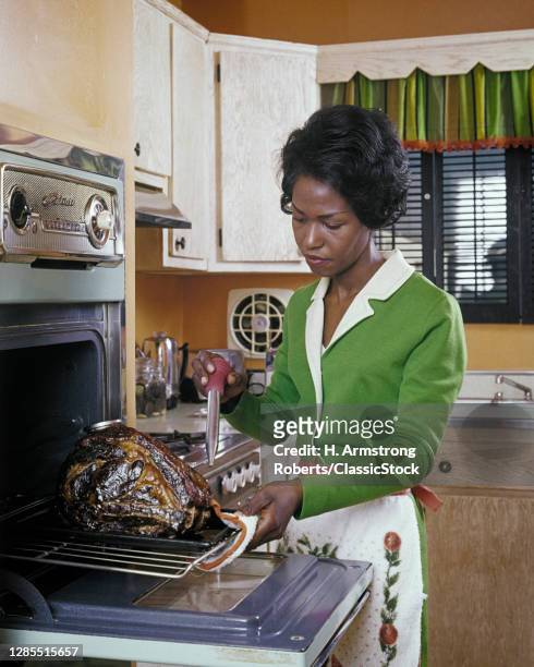 1980s African-American Woman Housewife Basting A Turkey In Electric Wall Oven