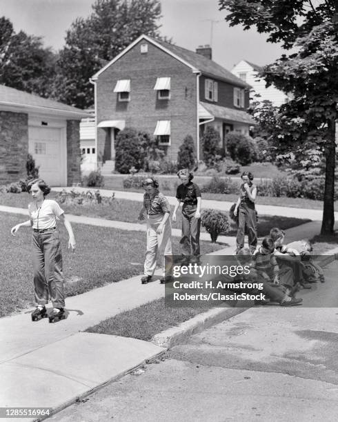 1950s Group Of Eight Boys And Girls Preteens And Teens Roller Skating On Suburban Street Sidewalk