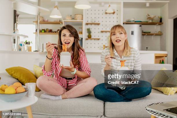 dos amigas están comiendo pasta en casa y viendo programas de televisión - catálogo fotografías e imágenes de stock