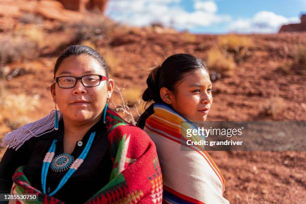 duas nativas americanas, irmãs navajo vestidas com roupas tradicionais, enroladas em um cobertor navajo sentado para trás, uma olhando para a frente, a outra olhando para o lado - reserva navajo - fotografias e filmes do acervo
