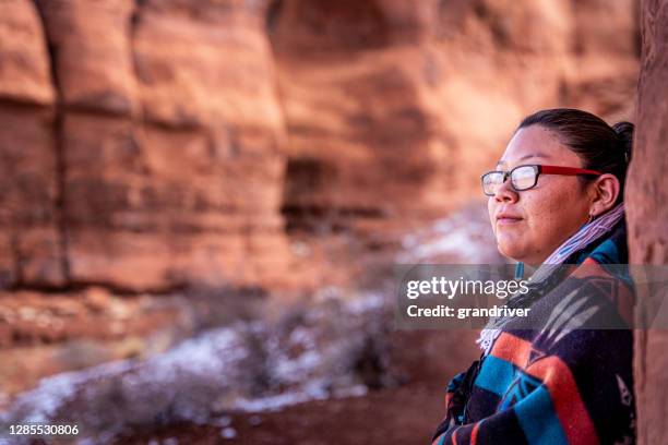 a closeup of a native american, navajo young woman wrapped up in a traditional navajo wool blanket and sitting in the iconic teardrop arch, monument valley, utah, arizona - mesa arizona stock pictures, royalty-free photos & images
