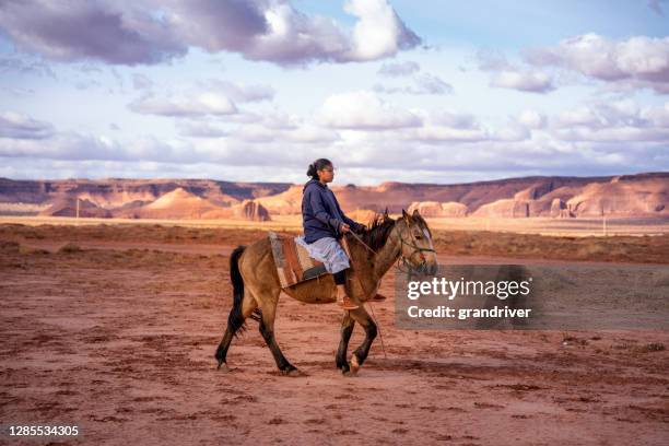 若いナバホティーンエイジガールライディング、彼女の馬はモニュメントバレー、アリゾナ州モニュメントバレー、モニュメントバレー部族公園でラクダビュート近くの砂漠の平原に - ute ストックフォトと画像
