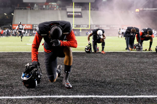 Several Cincinnati Bearcats players kneel to pray in the end zone prior to the start of the game against the East Carolina Pirates at Nippert Stadium...