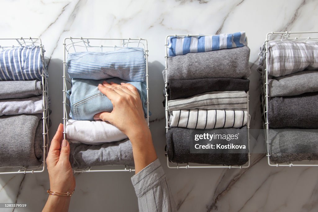 Neatly folded clothes and pyjamas in the metal mesh organizer basket on white marble table