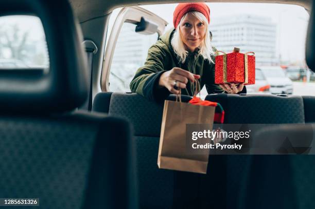 una giovane donna sorridente che impacchetta i regali di natale in un bagagliaio d'auto - car wrapping foto e immagini stock