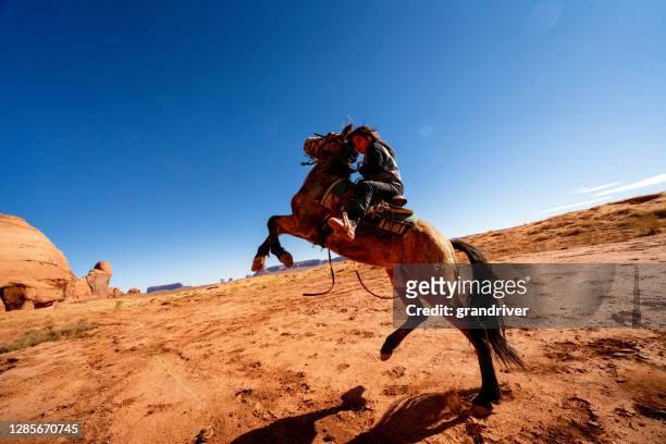a young navajo boy riding, his horse bucking on the desert plain in monument valley, arizona, monument valley tribal park - horseback riding arizona stock pictures, royalty-free photos & images