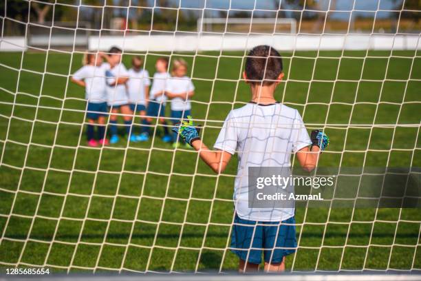 young boy footballer defending goal during practice drill - boy goalie standing in front of goal net stock pictures, royalty-free photos & images