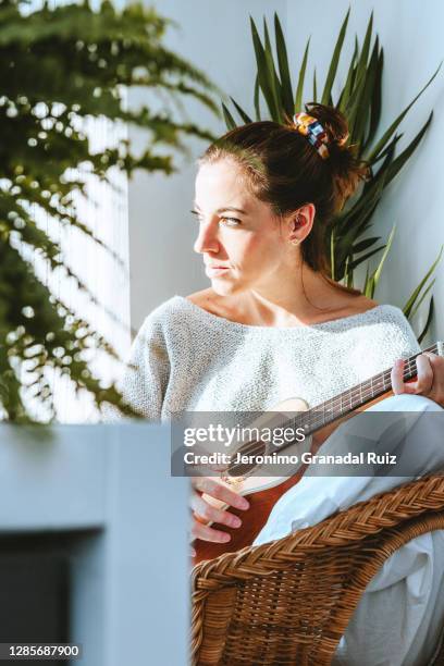 young woman playing ukulele at home while sunbathing - ukulele stock-fotos und bilder