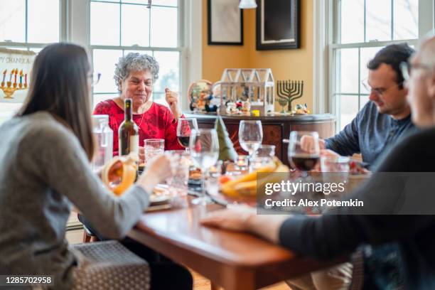two-generation multicultural family, the senior couple with adult kids, gathered together and have the holiday dinner in the living room decorated for both christmas and hanukkah. - jewish religion stock pictures, royalty-free photos & images