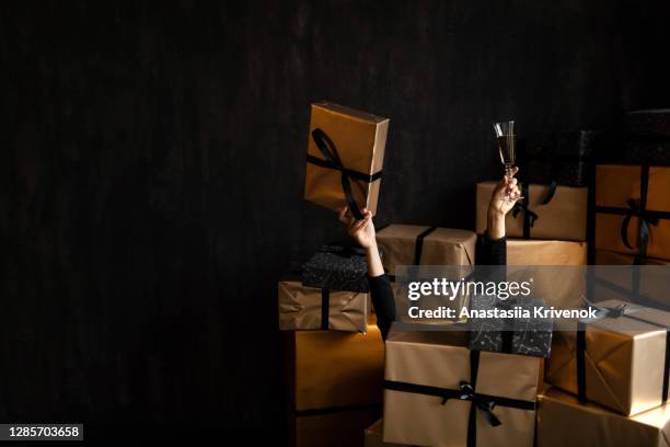 female hands stick out of the christmas stack of golden gifts. - black craft paper stock pictures, royalty-free photos & images