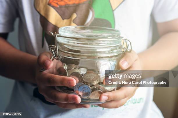 young child holding coins jar - charity education stock-fotos und bilder