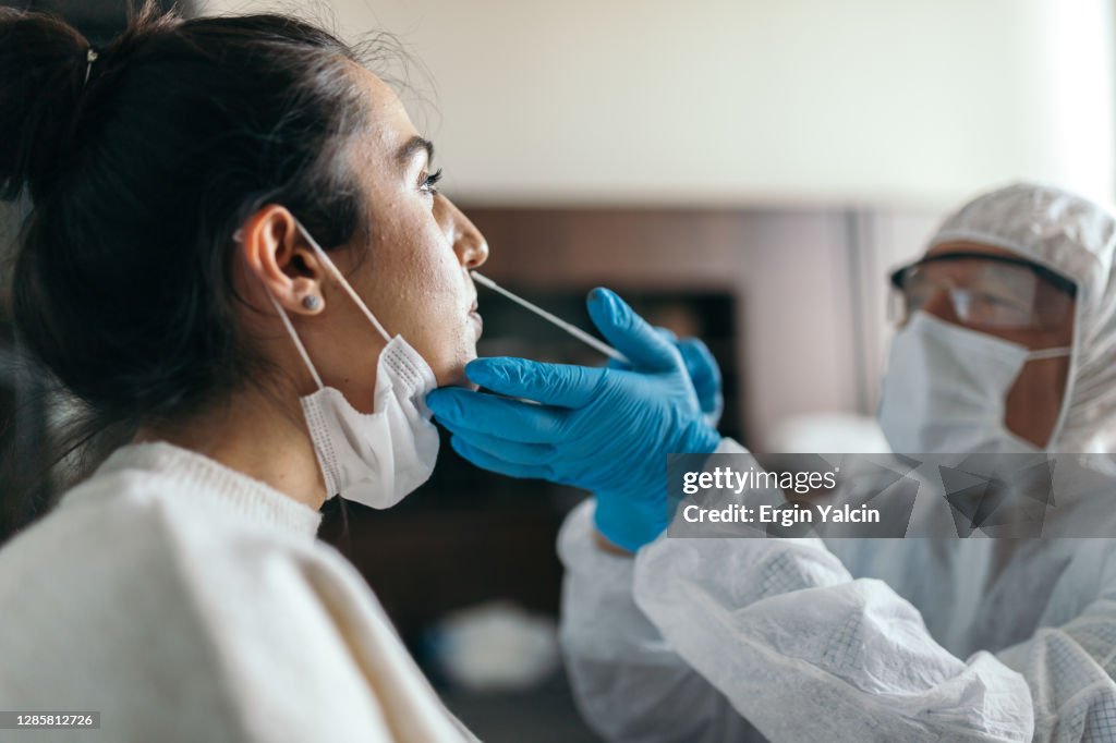 Médico en ropa de trabajo protectora tomando la prueba de hisopo de la nariz de la mujer joven