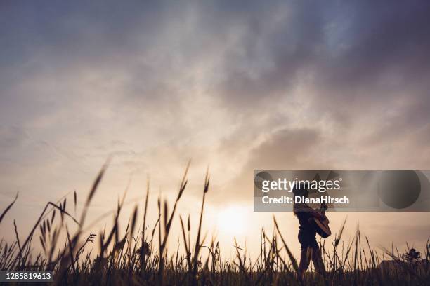 halbsilhouette eines cowgirls mit gitarre in der landschaft während des sonnenaufgangs - country and western music stock-fotos und bilder