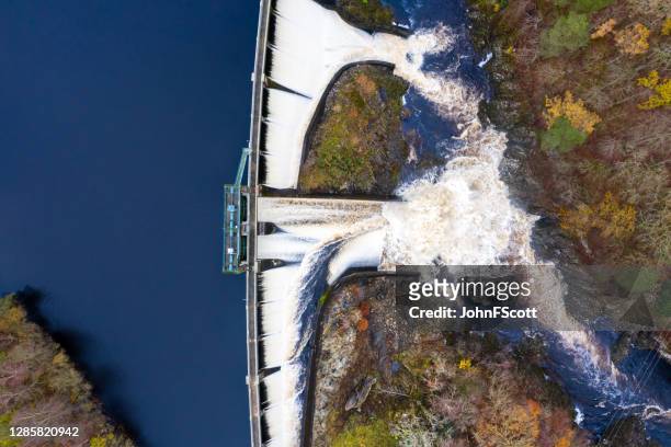 the view from a drone directly above water flowing over a hydro electric dam on an overcast day in dumfries and galloway south west scotland - hydroelectric power stock pictures, royalty-free photos & images