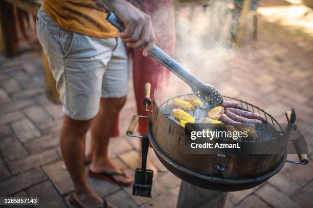 young male barbecuing chicken and sausage - courtyard stock pictures, royalty-free photos & images
