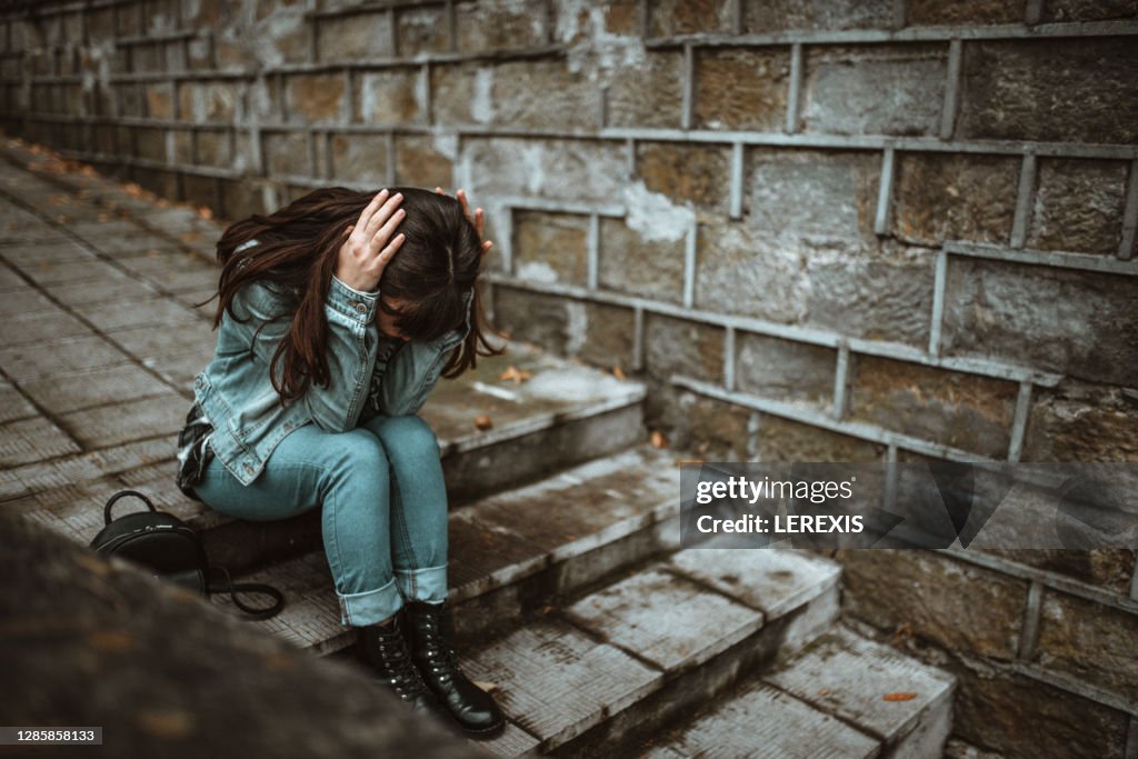 A sad young woman sitting on the stairs in the park and looking down