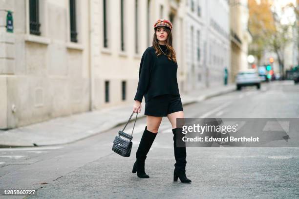 Sara Carnicella wears a red checked beret hat from Anthony Peto, a black oversized pullover from Natan, a black leather studded Valentino Rockstud...