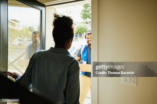 woman opening front door of home to receive package from smiling delivery driver - consegna a domicilio foto e immagini stock