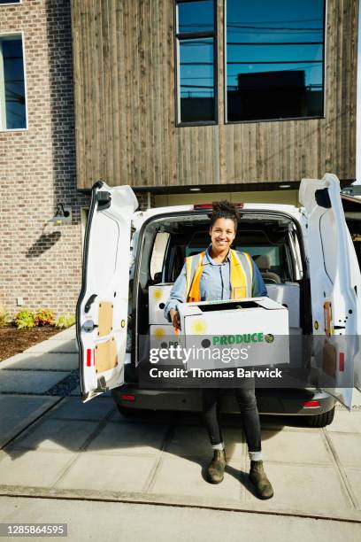 portrait of smiling female delivery driver standing at back of van holding fresh organic produce box during delivery at home - delivery truck stock pictures, royalty-free photos & images