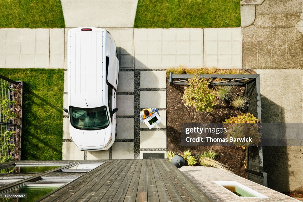 Overhead view of female delivery driver carrying produce box to front door of home