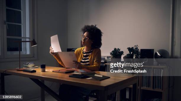 working from home late at night: a young african american woman sitting in her home office and reading documents - business people and paper imagens e fotografias de stock