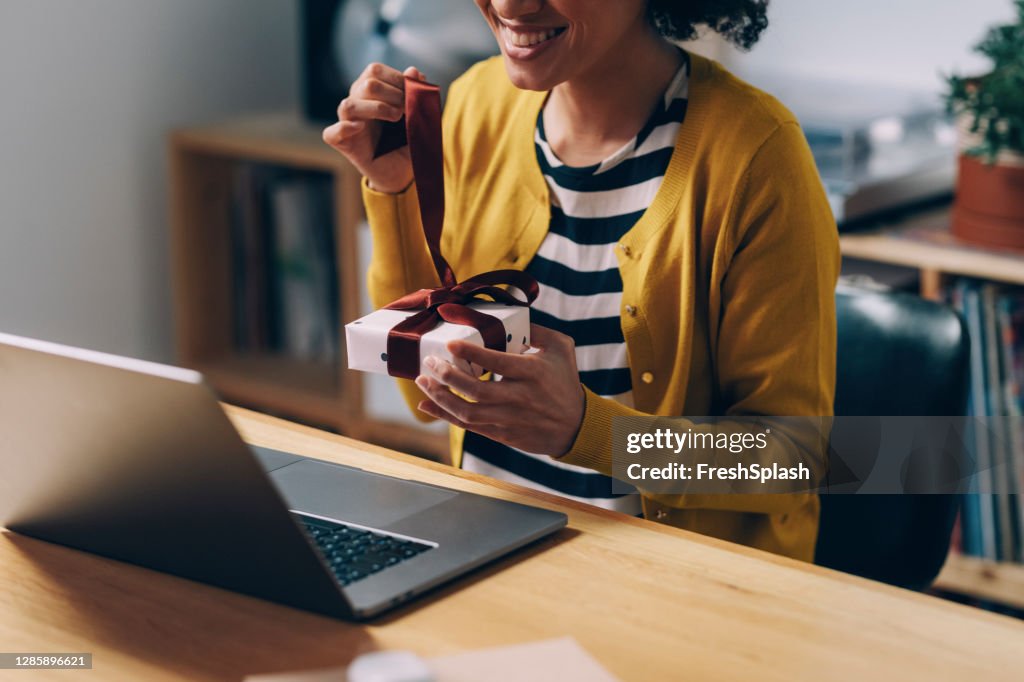 Celebrating from Home: an Anonymous Happy African American Woman Opening a Christmas Present During a Video Call on her Laptop Computer
