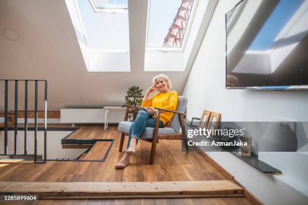 hogere vrouw die van alleen tijd met haar digitale tablet in een gezellig hoekje geniet - nook architecture stockfoto's en -beelden