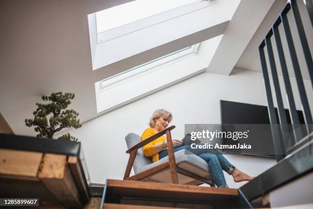 hogere vrouw die van alleen tijd met haar digitale tablet in een gezellig hoekje geniet - nook architecture stockfoto's en -beelden