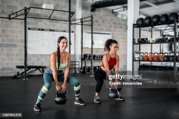 zwei sportlerinnen trainieren mit kettlebells im fitnessstudio - women gym stock-fotos und bilder