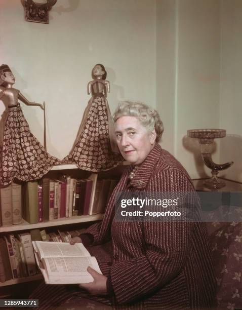 English writer and novelist Agatha Christie seated reading by a bookshelf of books in a living room at her home, Winterbrook House near Wallingford,...