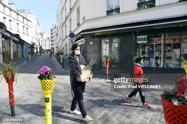 Une femme avec un masque porte un carton de courses, un enfant marche en respectant la distance sociale dans la rue le 31 mars 2020, Paris, France.