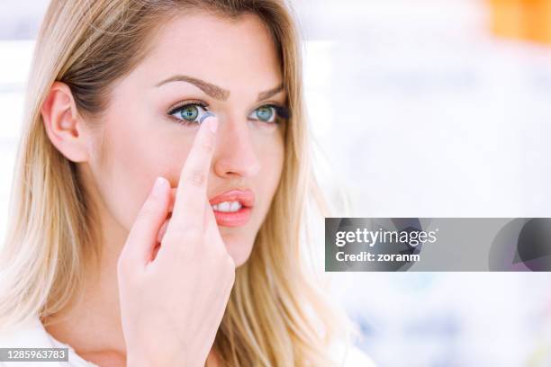 young woman holding blue contact lens on her finger and moving toward her eye - lente de contacto imagens e fotografias de stock