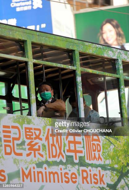 Passager masqué pour se protéger du virus Corona à la fentre d'un tramway traversant le quartier touristique de Causeway Bay et publicité "Minimise...