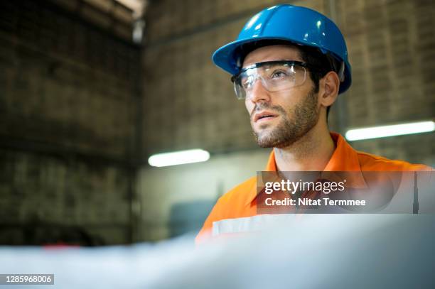 portrait of construction worker reading blueprints while looking around at site. - building confidence stock pictures, royalty-free photos & images