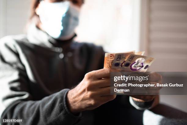 a man wearing a face mask, holding five and ten pound notes - covid economy stock pictures, royalty-free photos & images