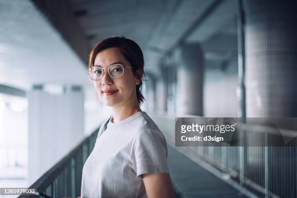 portrait of confident and successful young asian businesswoman looking at camera with smile, standing against urban bridge in the city - asiático e indiano imagens e fotografias de stock
