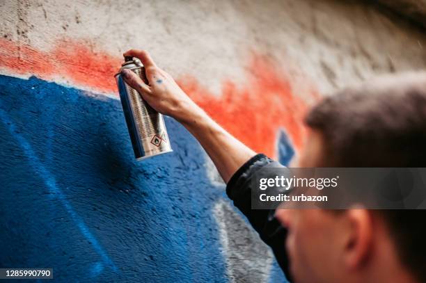 hombre pintando grafitis en la pared - oficio artístico fotografías e imágenes de stock